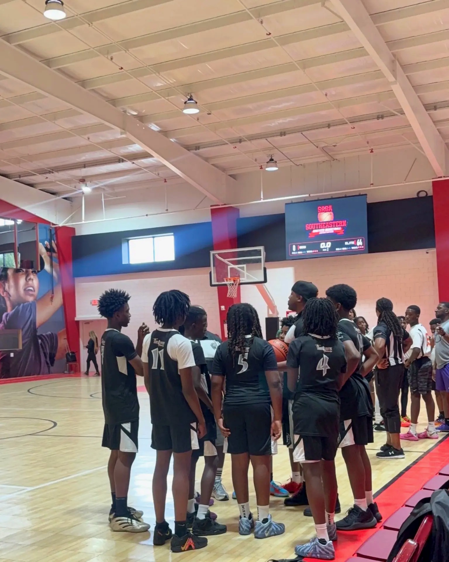 N.O.W. Wolves players in black uniforms gathered in a team huddle on the gym floor