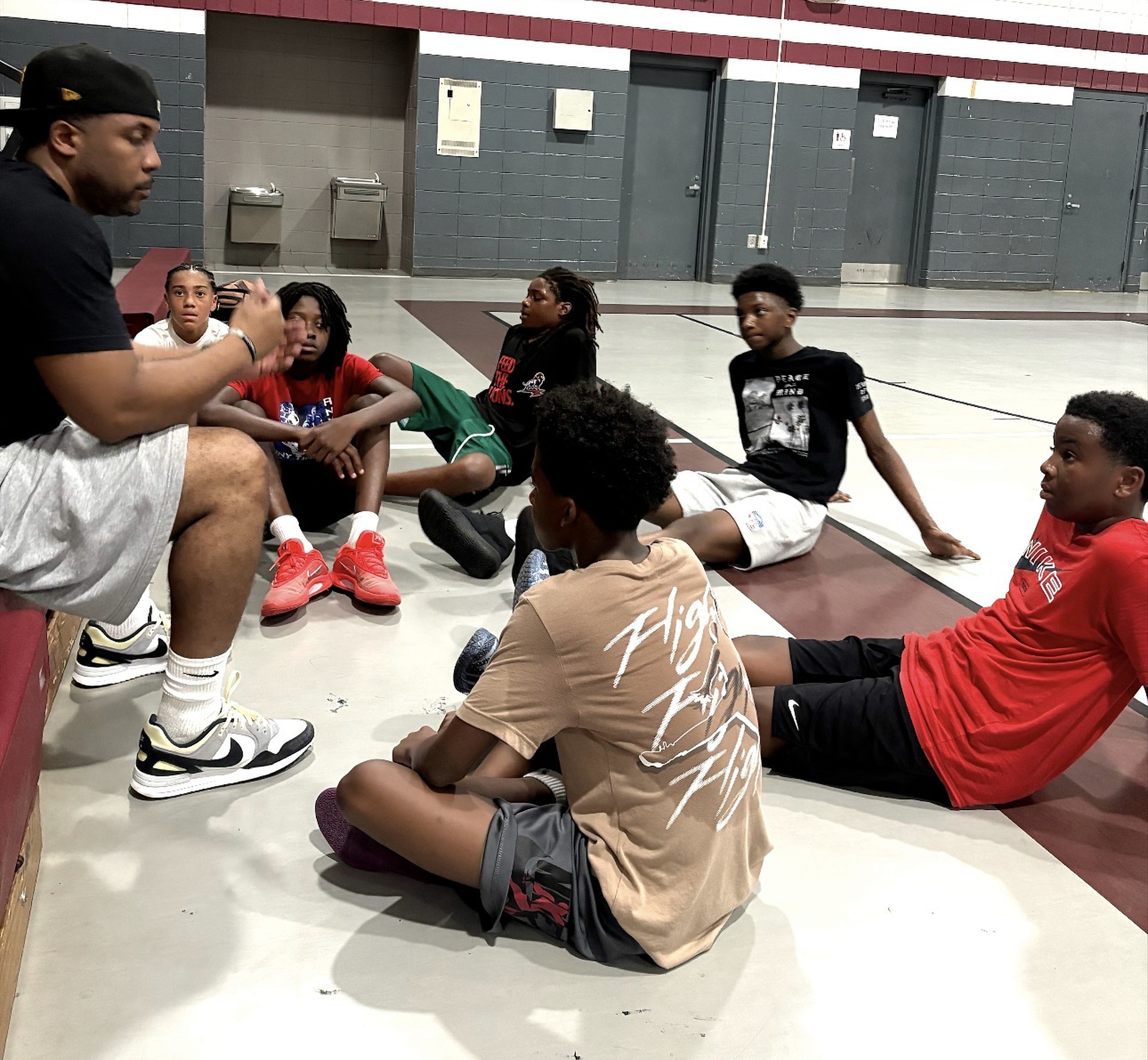A coach speaking with players seated in a circle on the gym floor
