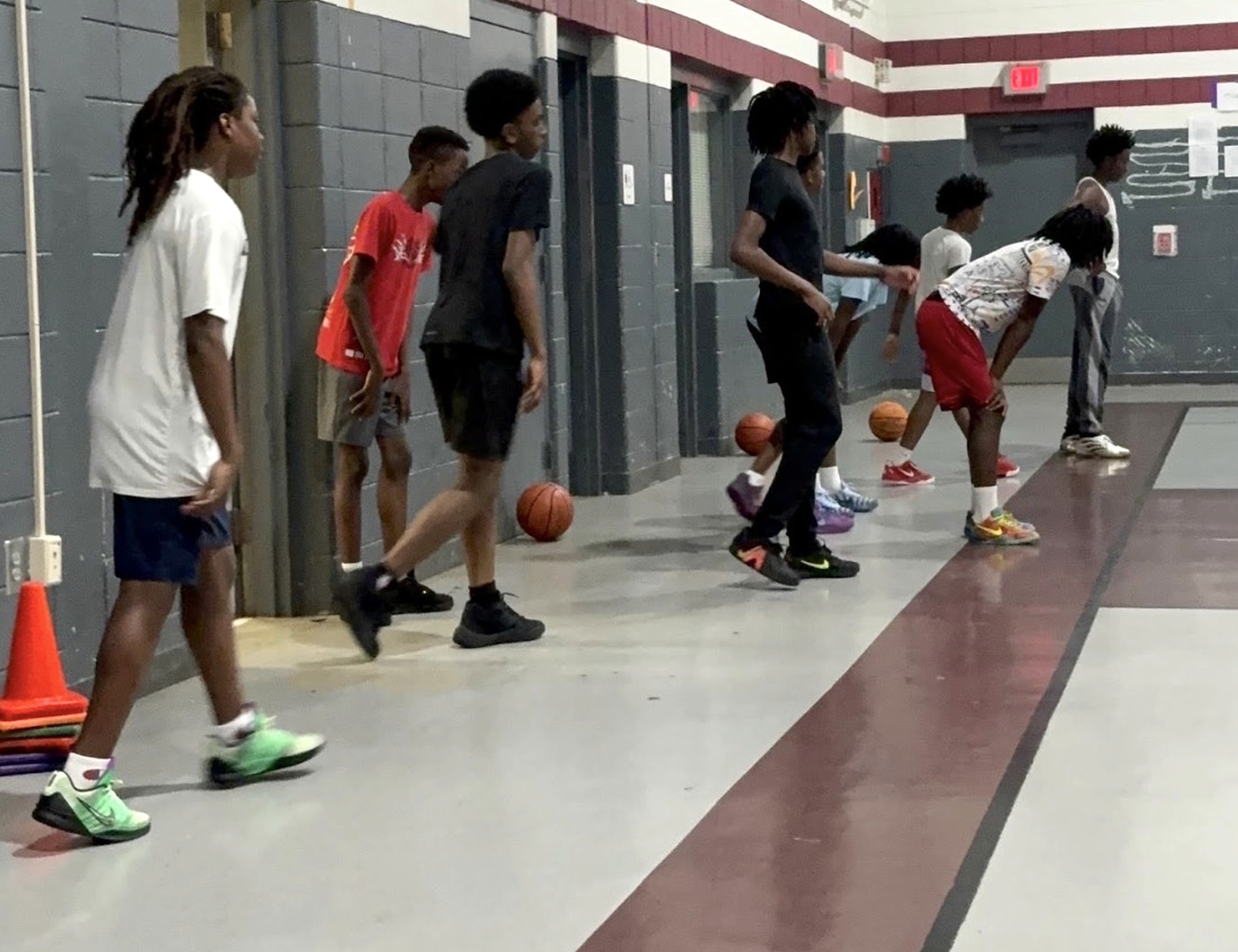 Players practicing basketball drills along the side of the gym